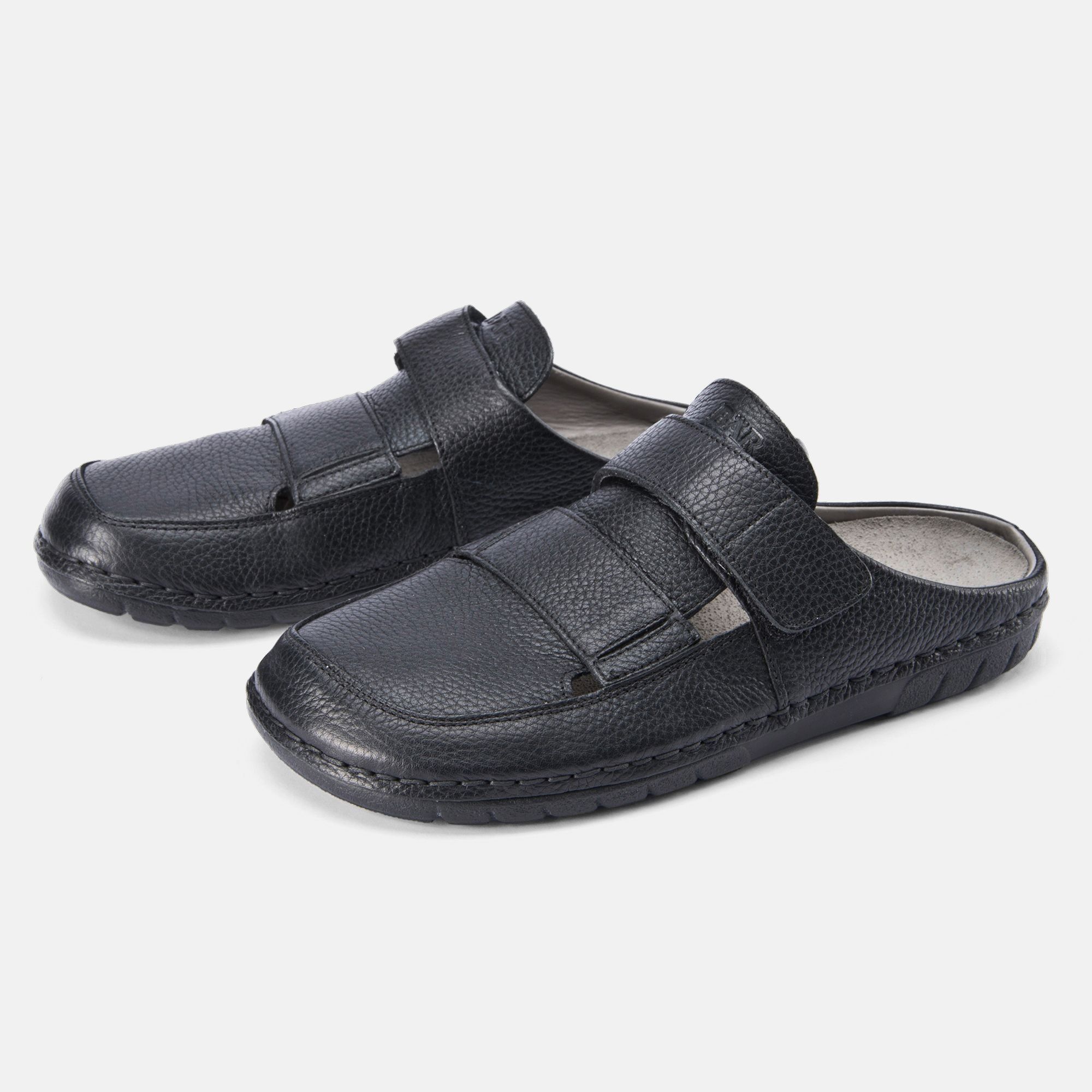 Schwarze Pantoletten mit Klettverschluss. Obermaterial Leder. Breite Form. Zwei Schuhe nebeneinander, leicht schräg gestellt.