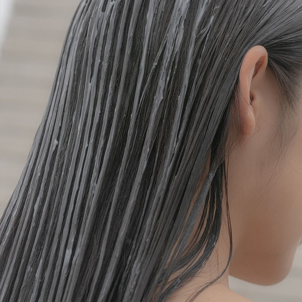 Nahaufnahme von Haar, das mit einer Creme bedeckt ist. Die Haare sind dunkel und nass.