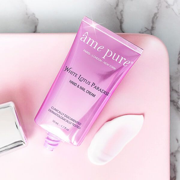 Roze handcrèmetube op roze dienblad. Crème wordt eruit geperst. Tekst: âme pure, White Lotus Paradise.