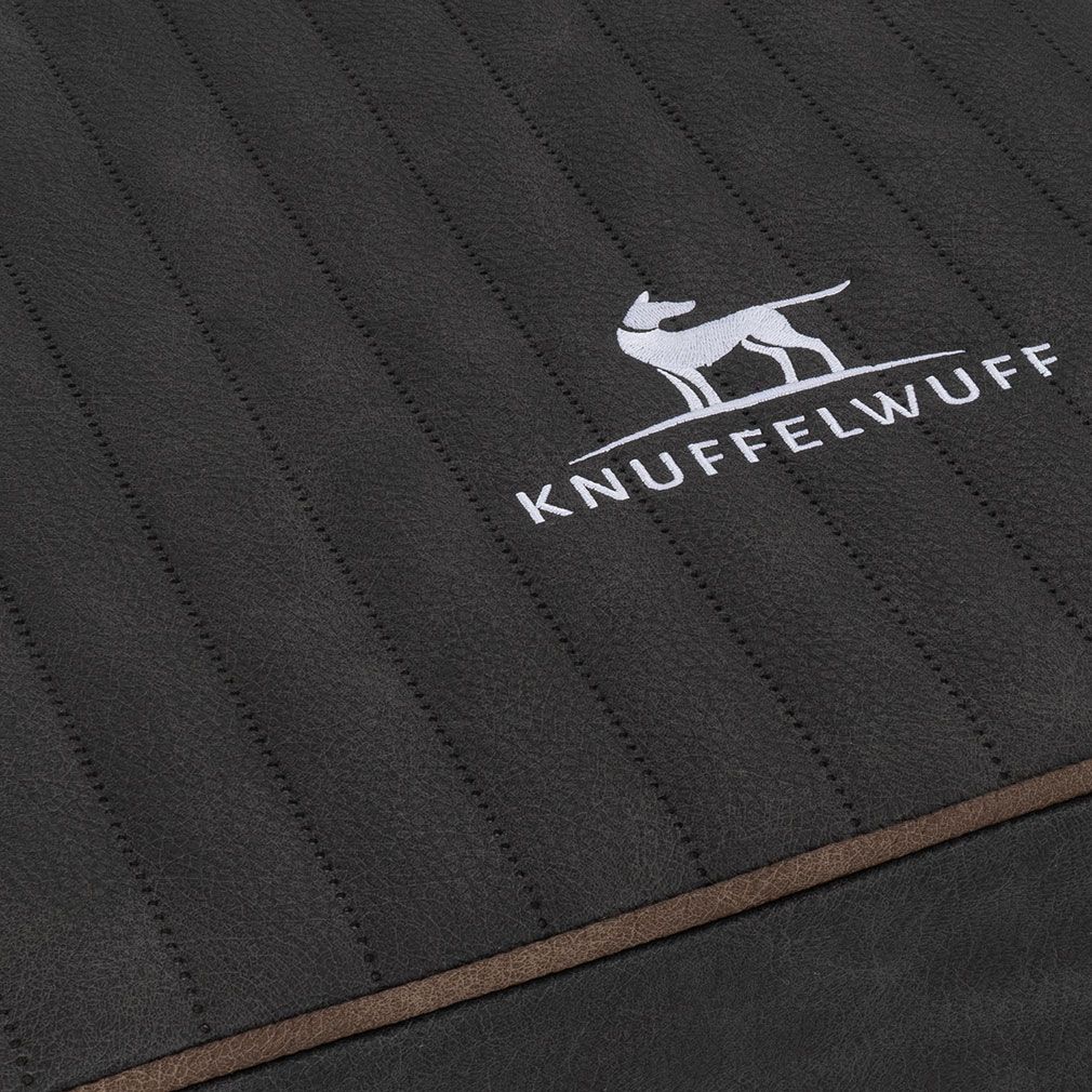 Detailansicht der orthopädischen Hundematte. Dunkelgraues, gestepptes Material. Knuffelwuff Logo und brauner Rand.