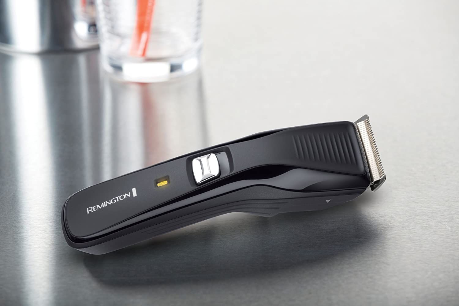 Schwarzer Haarschneider auf einer Metalloberfläche. Marke: Remington. Mit Ein-/Ausschalter und Ladeanzeige.