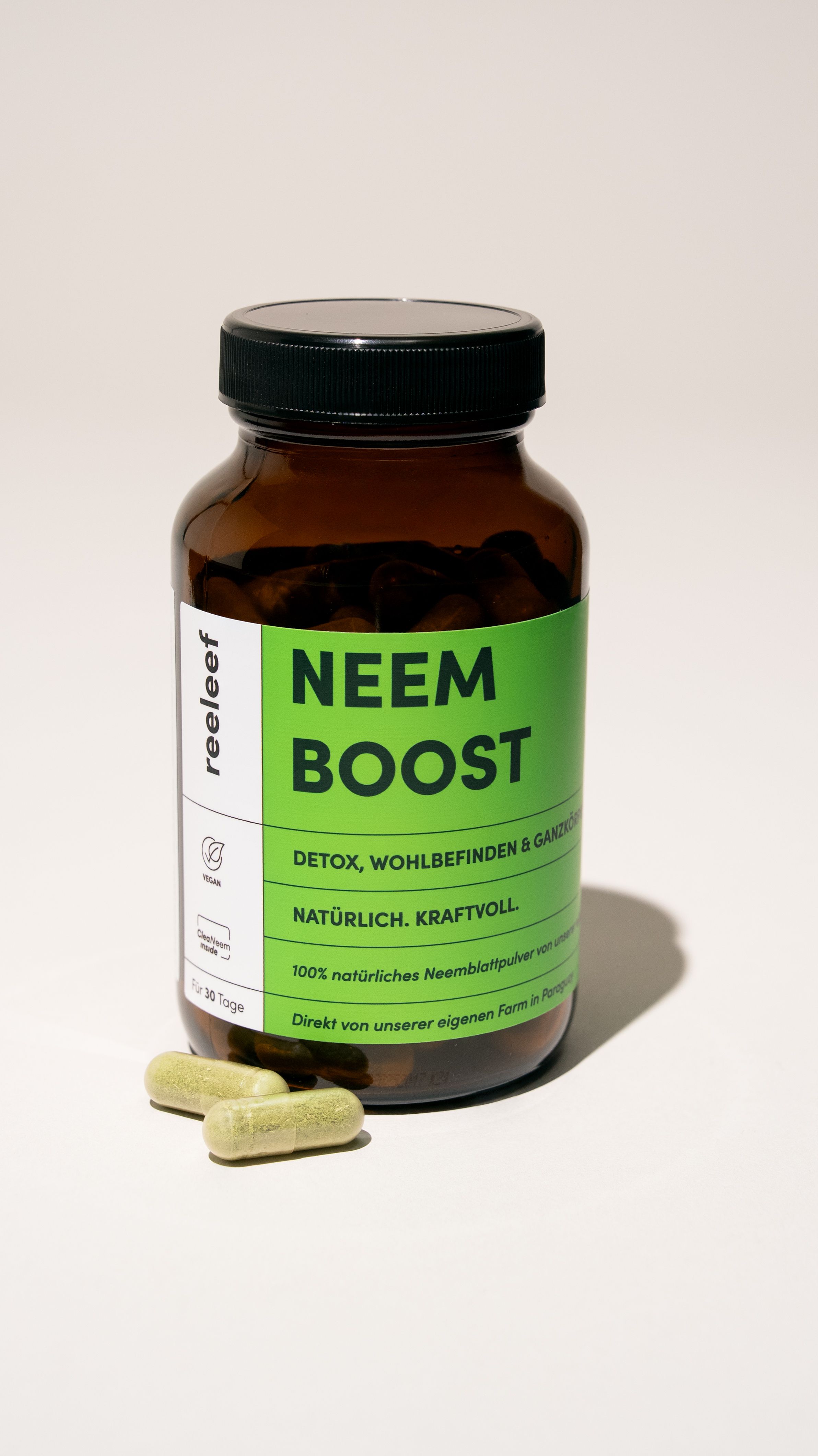 Braune Glasflasche mit grünem Etikett. Aufschrift: NEEM BOOST. Daneben drei grüne Kapseln.