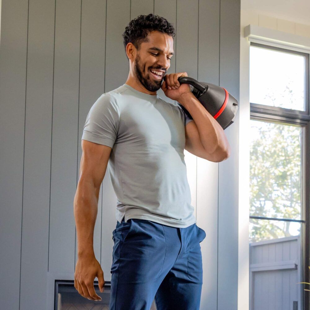 Mann mit Kettlebell. Schwarze Kettlebell mit rotem Band. Bowflex-Logo sichtbar.
