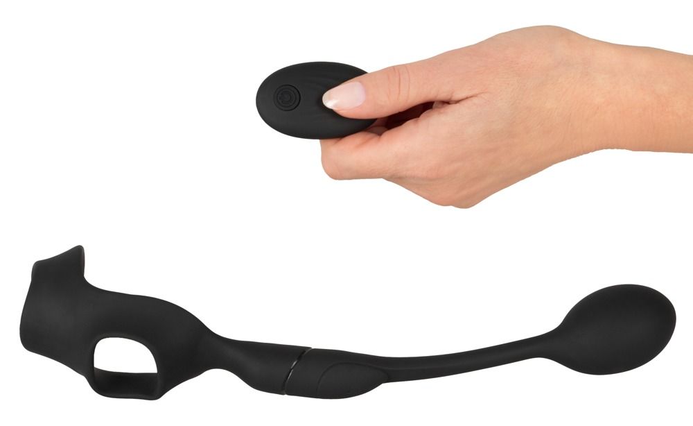 Hand hält Fernbedienung. Schwarzer Penisring mit Hodenring und Analplug daneben.