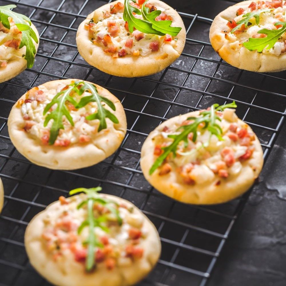 Kleine Flammkuchen auf schwarzem Gitter. Belegt mit Speck, Zwiebeln und Rucola. Mehrere Flammkuchen.