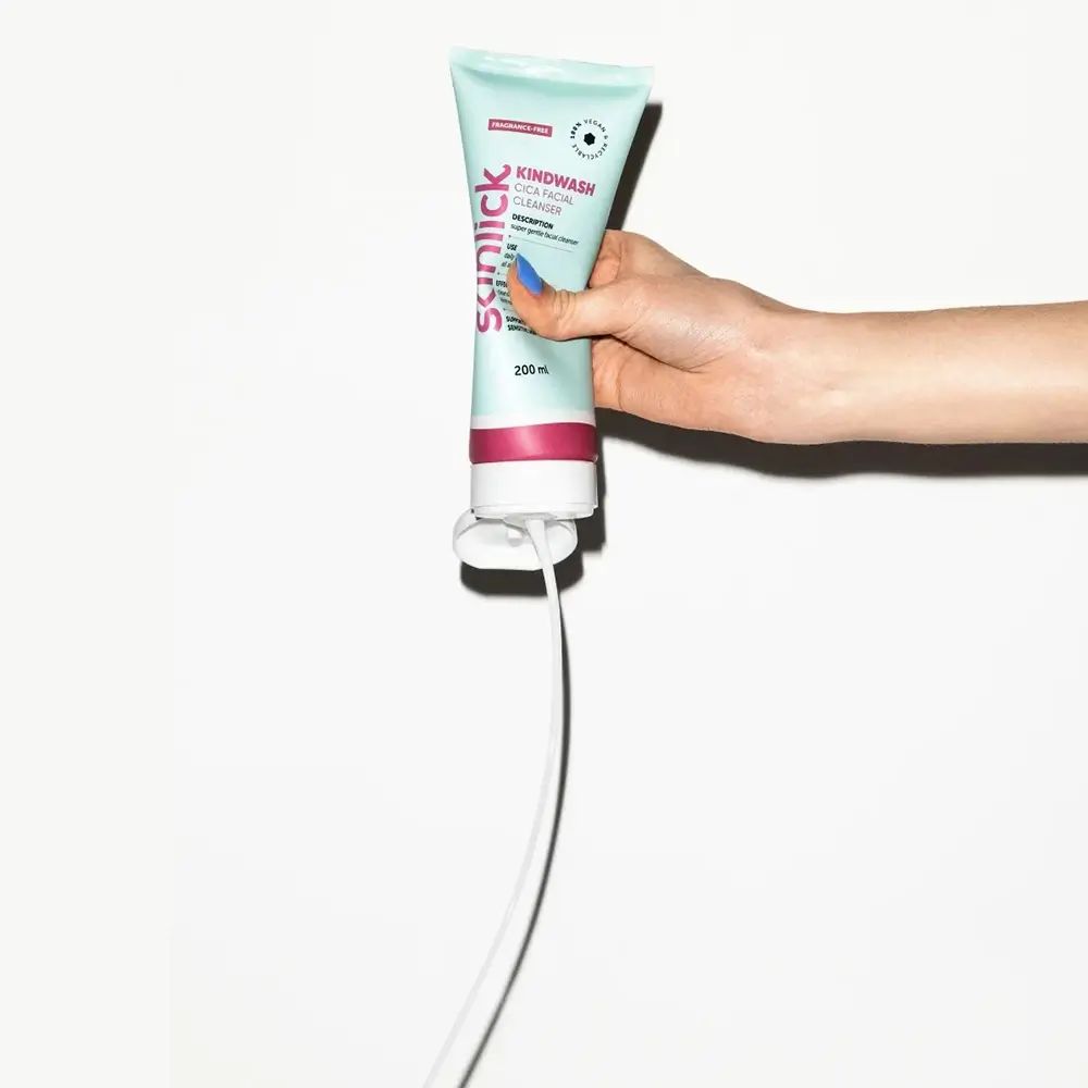Hand hält Tube. Aufschrift: Kindwash Cica Facial Cleanser. Tube wird ausgedrückt. Weißer Hintergrund.