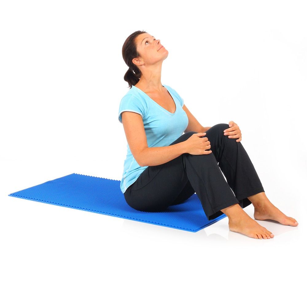 Blaue Massagematte. Frau sitzt, Beine angewinkelt, Blick nach oben gerichtet.