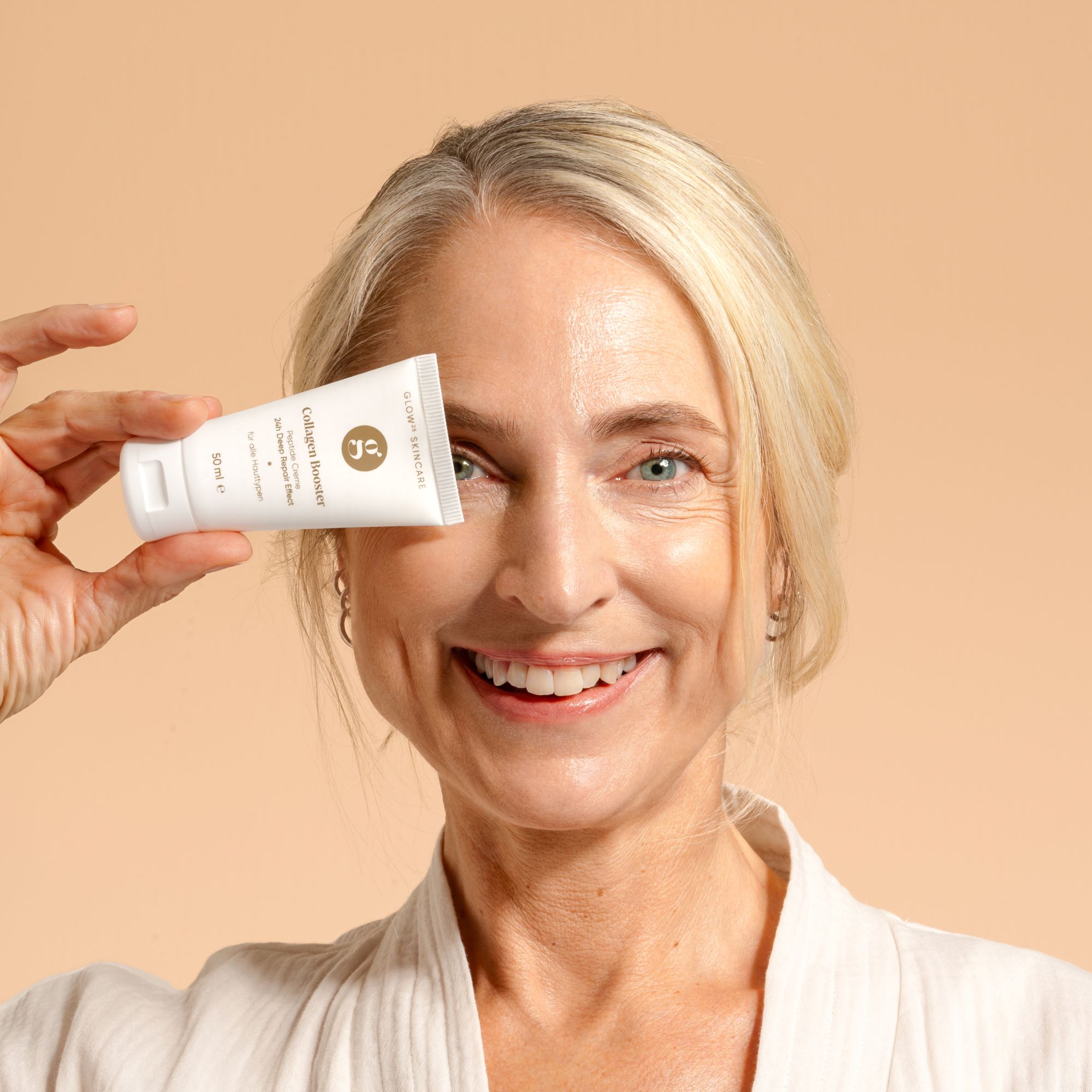 Frau hält Creme-Tube vor dem Auge. Sie lächelt.