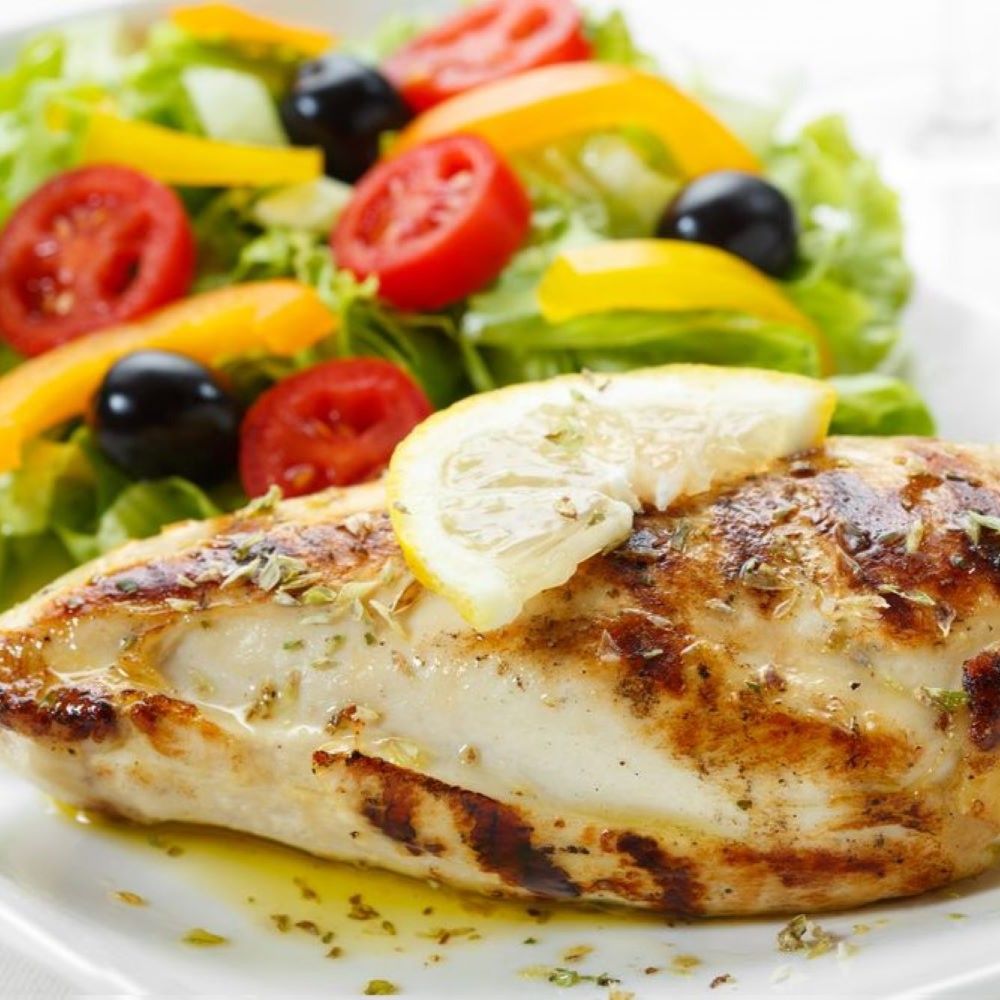 Gegrilltes Hähnchenbrustfilet mit Salat. Auf weißem Teller. Hähnchen mit Zitrone, Salat mit Tomaten, Paprika, Oliven.