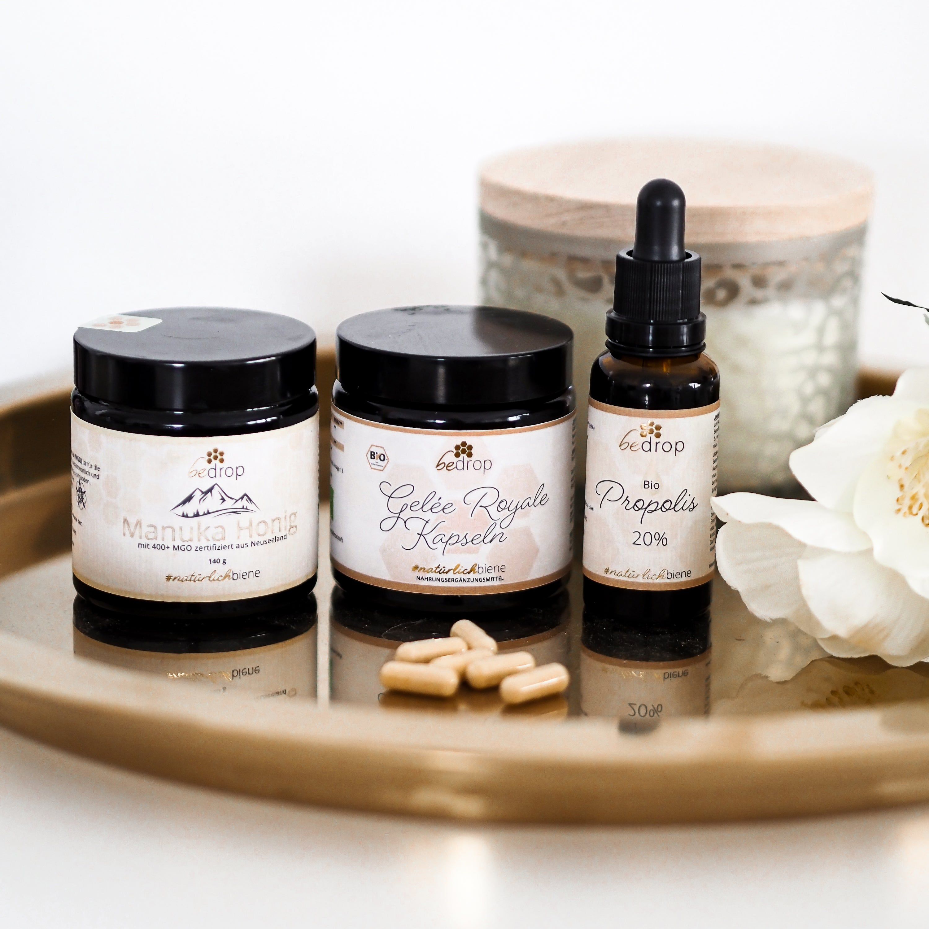 Goldene Tablett mit drei Gläsern: Manuka Honig, Gelee Royale Kapseln und Propolis Tinktur. Daneben Kapseln.