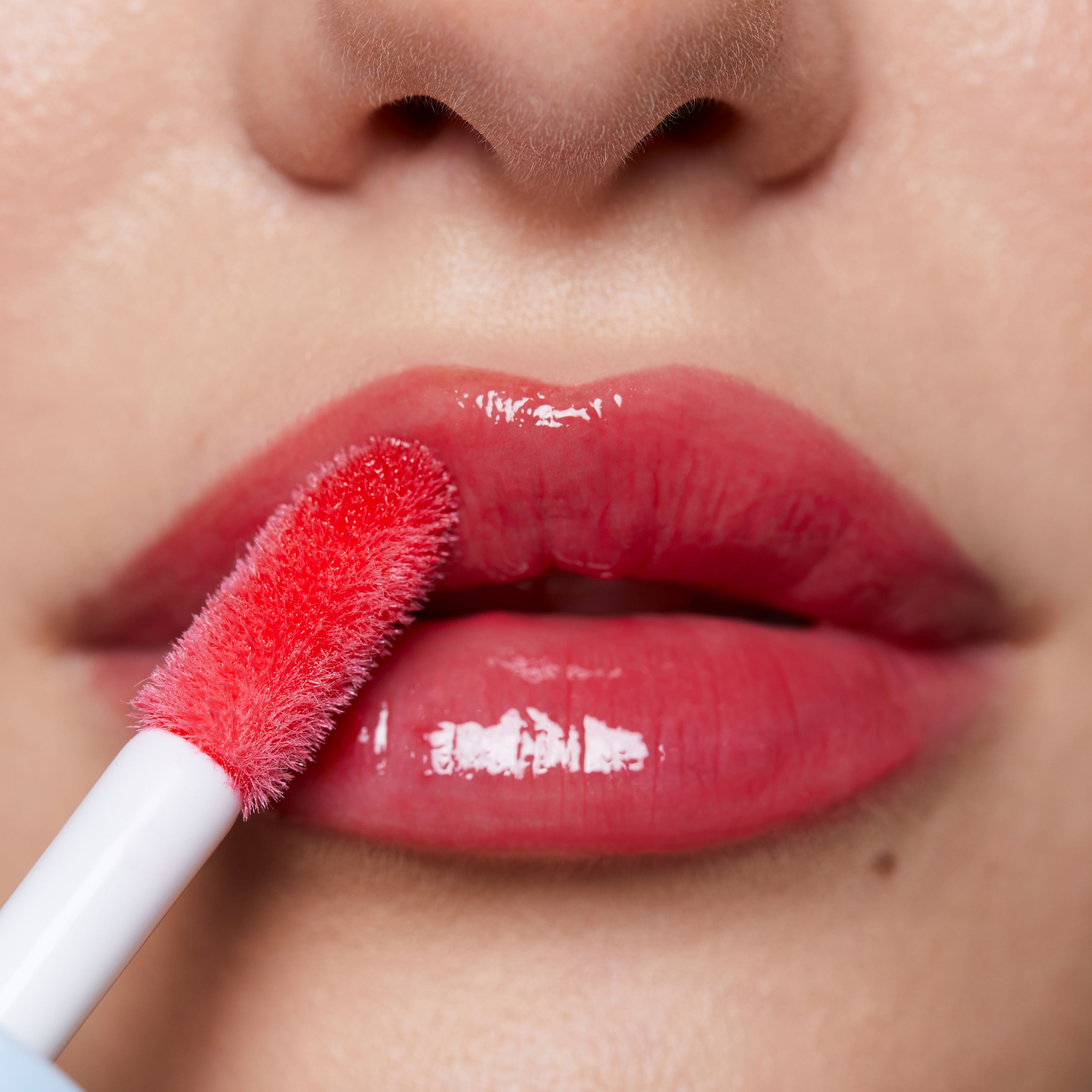 Nahaufnahme von Lippen mit rotem Lipgloss. Ein Applikator wird verwendet.
