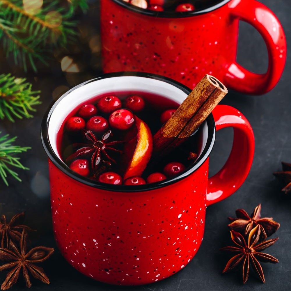 Zwei rote Tassen mit Glühwein. Zimtstange, Orangenscheibe und Sternanis in jeder Tasse.