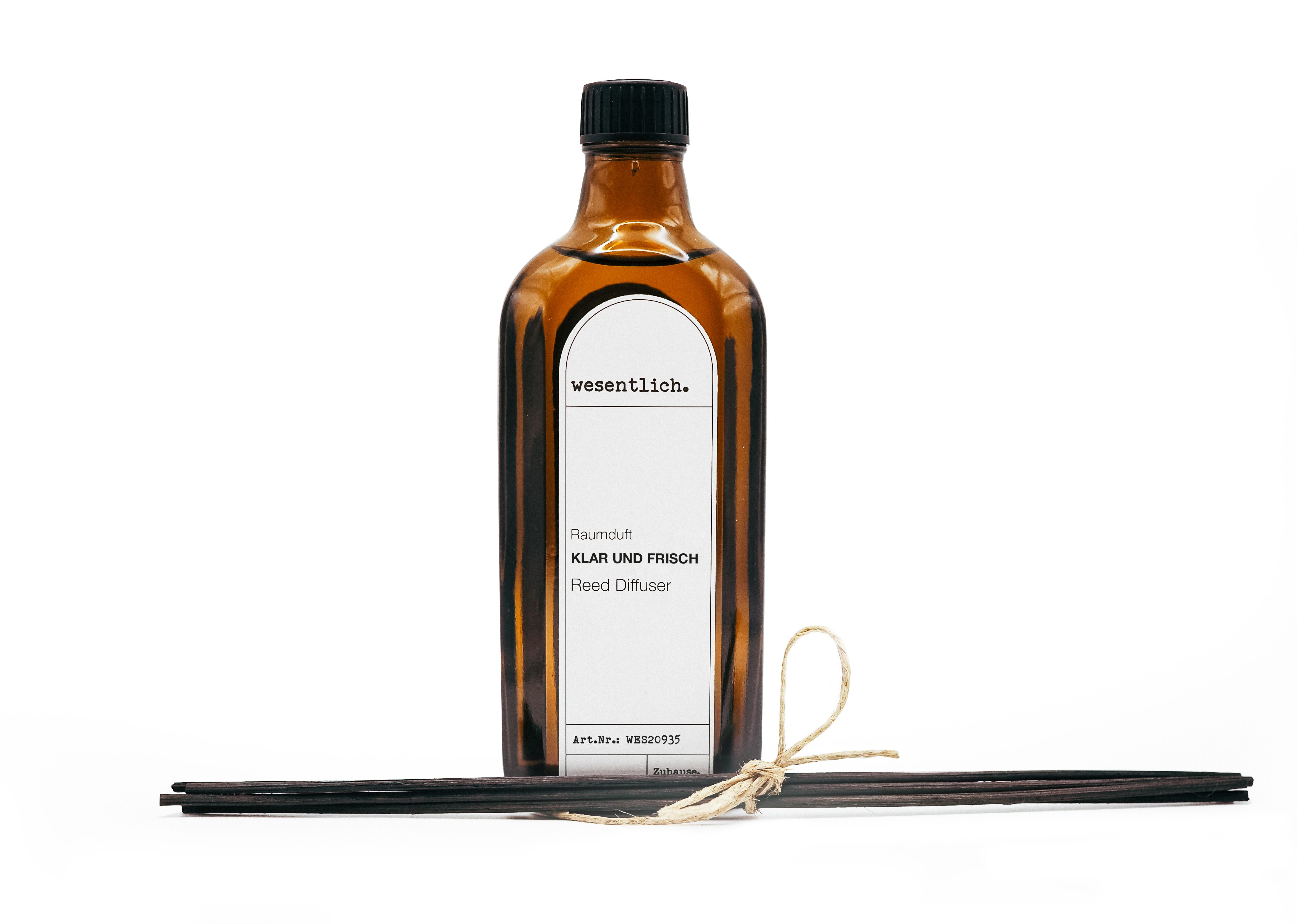 Braune Glasflasche mit schwarzem Deckel und weißem Etikett. Enthält schwarze Stäbchen, gebunden mit Kordel.