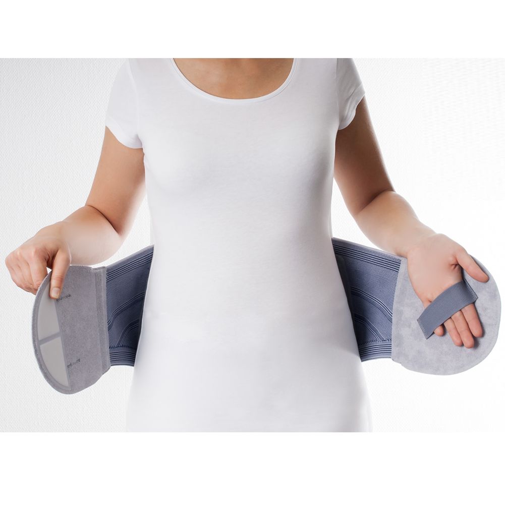 Person trägt eine graue OFA Dynamics LWS Bandage. Die Bandage wird um den Bauch gelegt und mit den Händen gehalten.