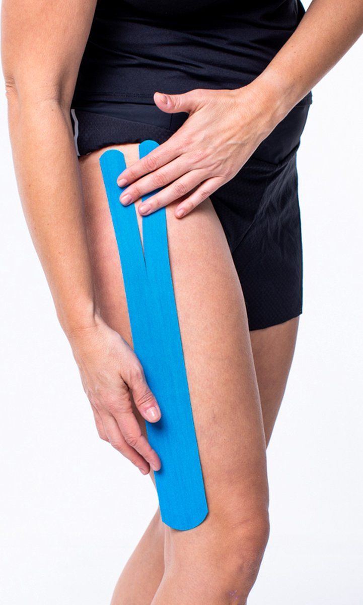 Blaues CureTape® Classic Kinesiotape auf Oberschenkel. Tape wird angebracht. Auf weißem Hintergrund.