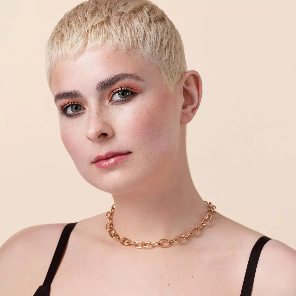 Goldfarbene Halskette mit ovalen Gliedern, getragen von einer Person mit kurzen blonden Haaren.
