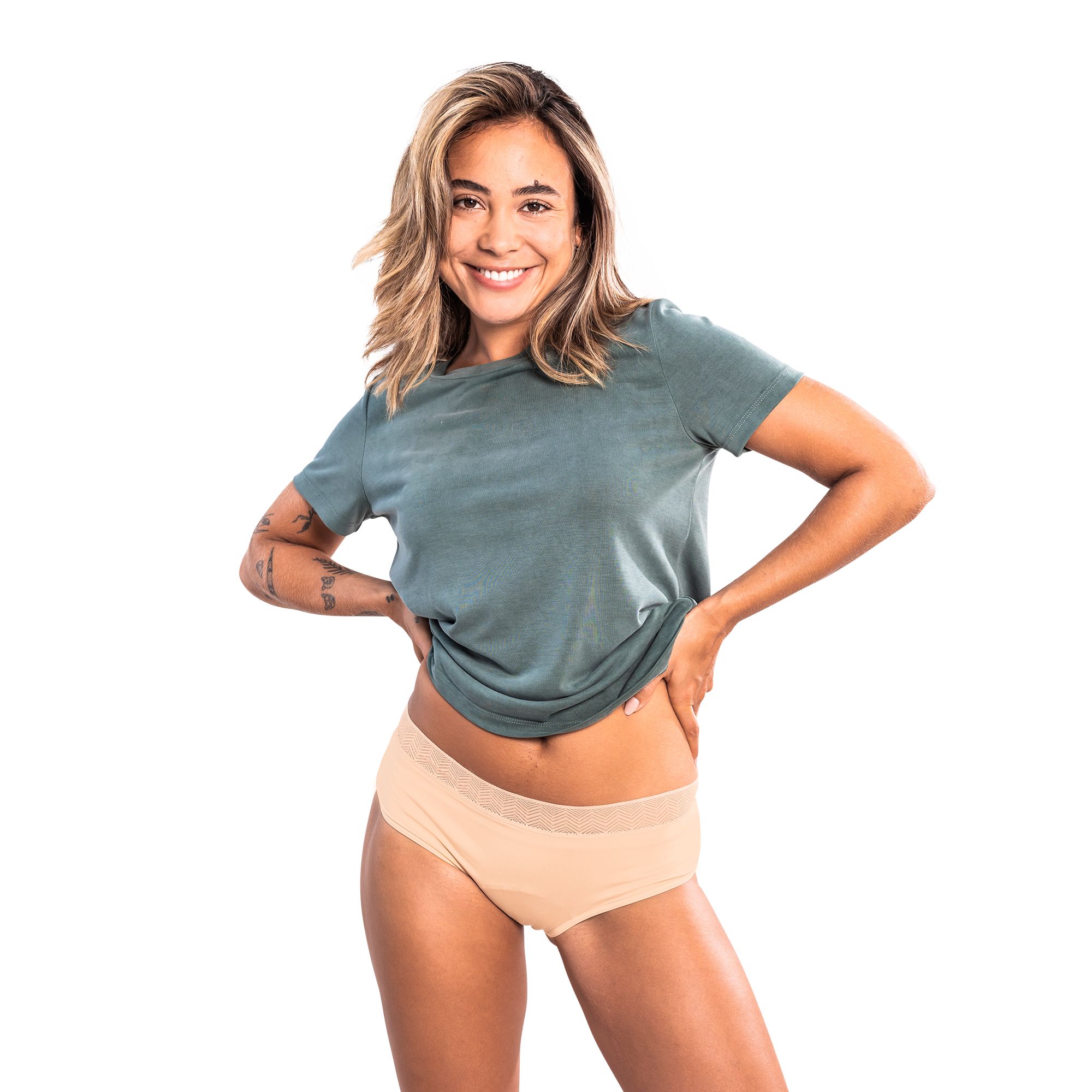 Beige Hipster-Slip. Frau mit Tattoo und grünem T-Shirt. Blick in die Kamera, Hände an der Hüfte.