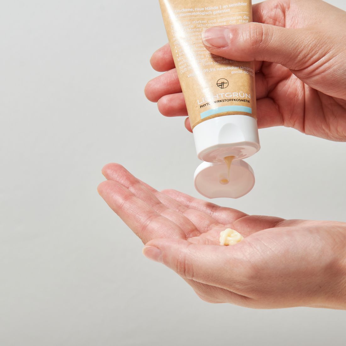 Handcreme wird aus einer Tube in eine Handfläche gegeben. Weiße Creme mit gelblichem Schimmer.