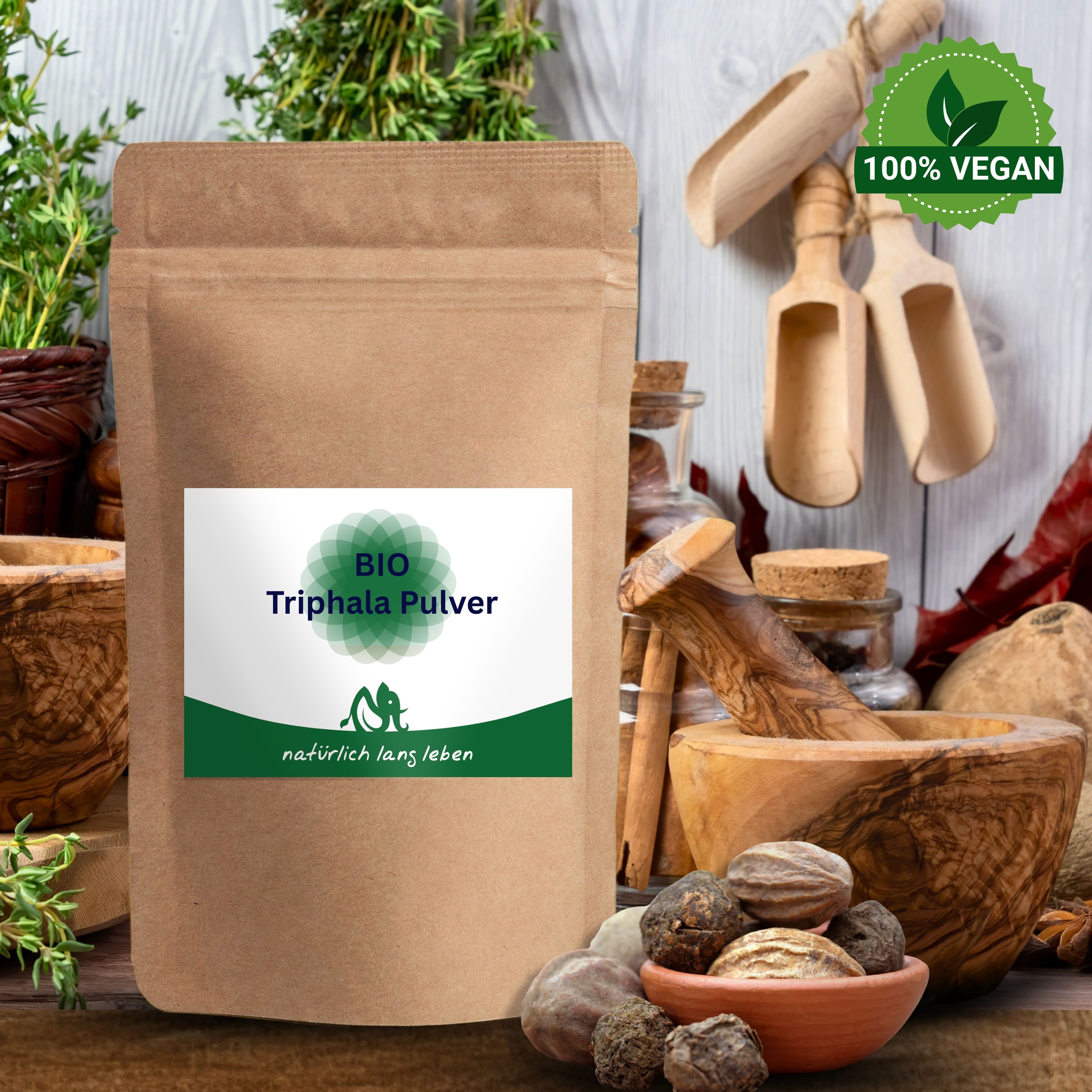 BIO Triphala Pulver Beutel, umgeben von Zutaten und Utensilien. Brauner Beutel mit grünem Etikett. Natürliche Umgebung.