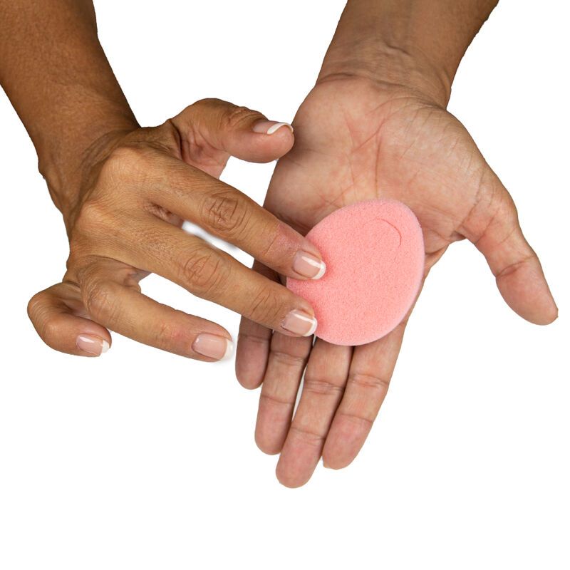 Hände halten einen rosa Schwamm. Der Schwamm ist rund und flach.