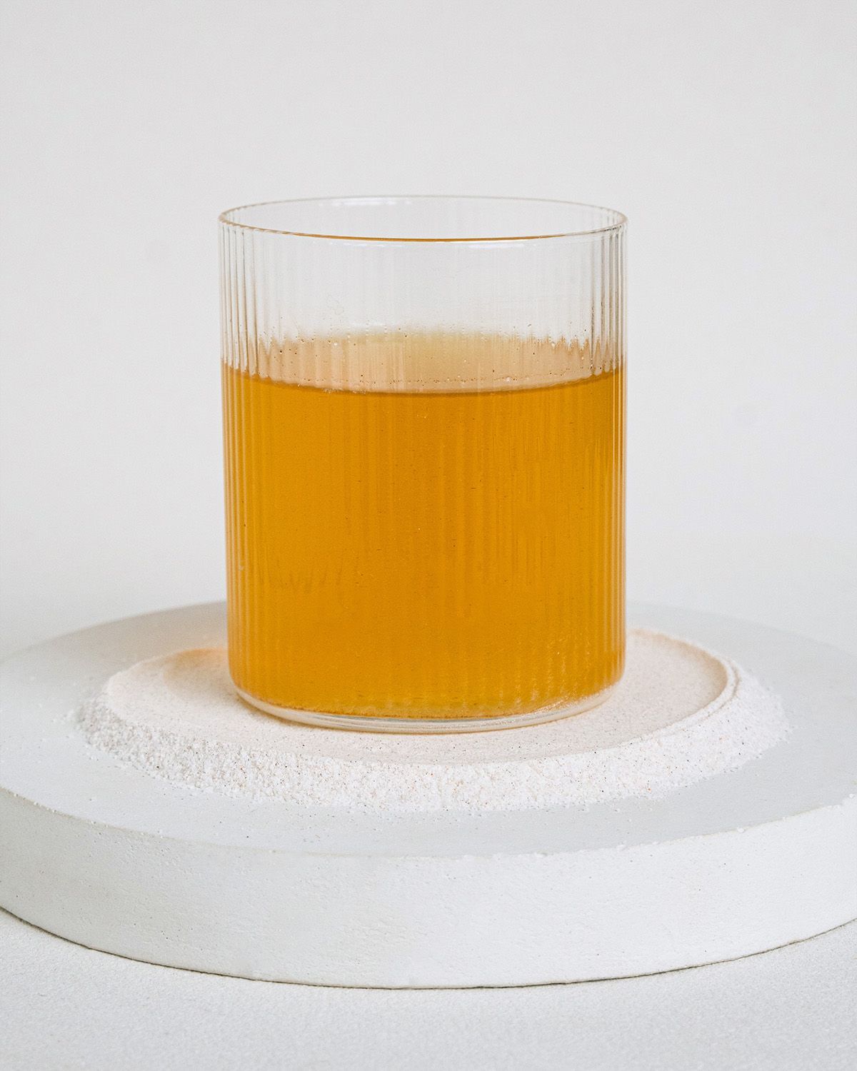 Ein Glas mit einem gelben Getränk, das auf einem weißen Podest steht.