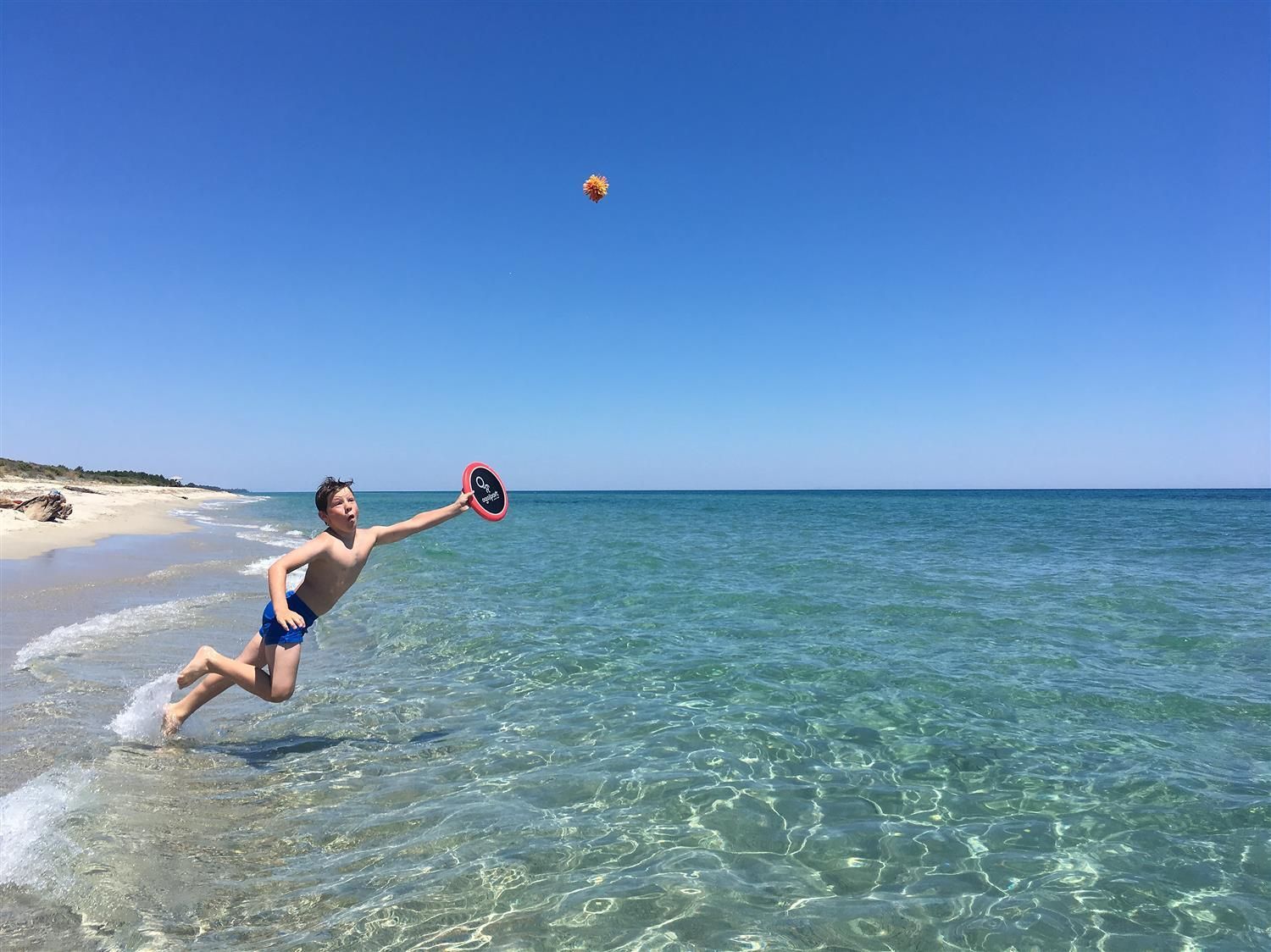 Ein Junge springt ins Meer, um eine Ogo Sport® Scheibe zu fangen. Blauer Himmel, klares Wasser.