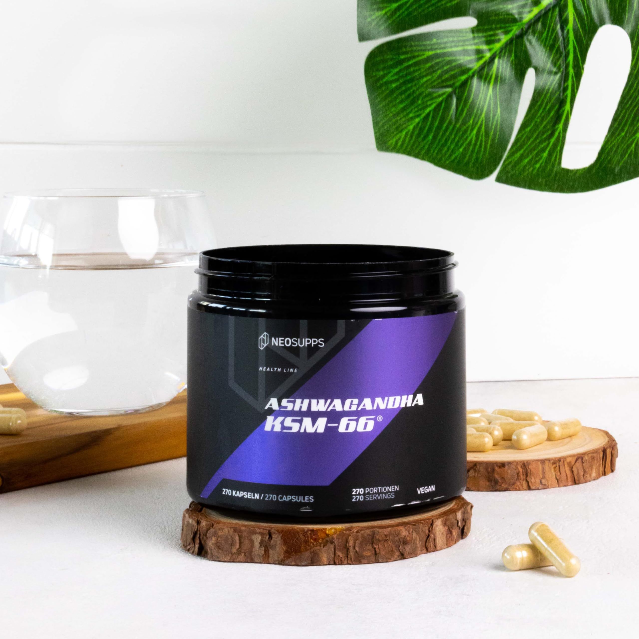 Schwarze Dose mit Aufschrift ASHWAGANDHA KSM-66. Auf einem Holzstück stehend. Daneben Kapseln und ein Glas Wasser.
