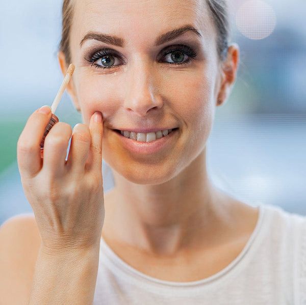 Frau trägt GRN Liquid Concealer auf. Sie lächelt. Der Applikator wird unter dem Auge verwendet.