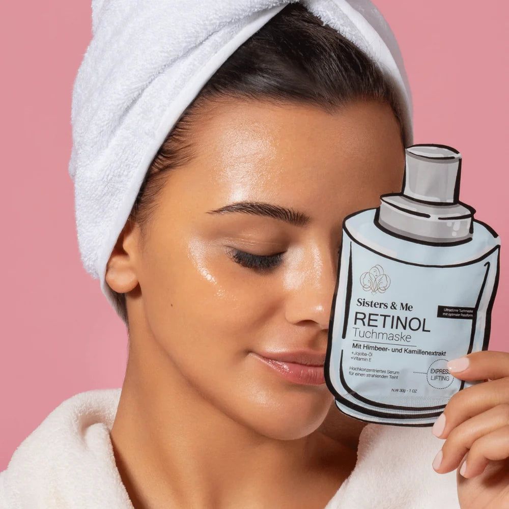 Frau mit Handtuch und Bademantel hält Retinol Tuchmaske. Gesicht mit Feuchtigkeit. Rosa Hintergrund.