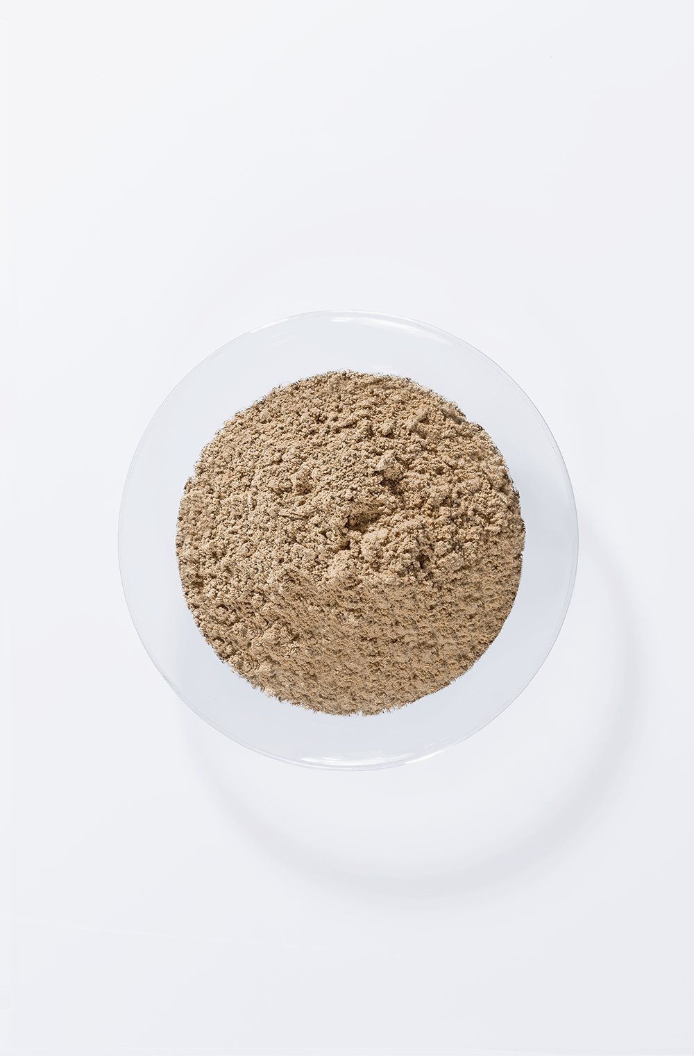 Braunes Pulver in einer transparenten Glasschale. Draufsicht auf weißem Hintergrund.