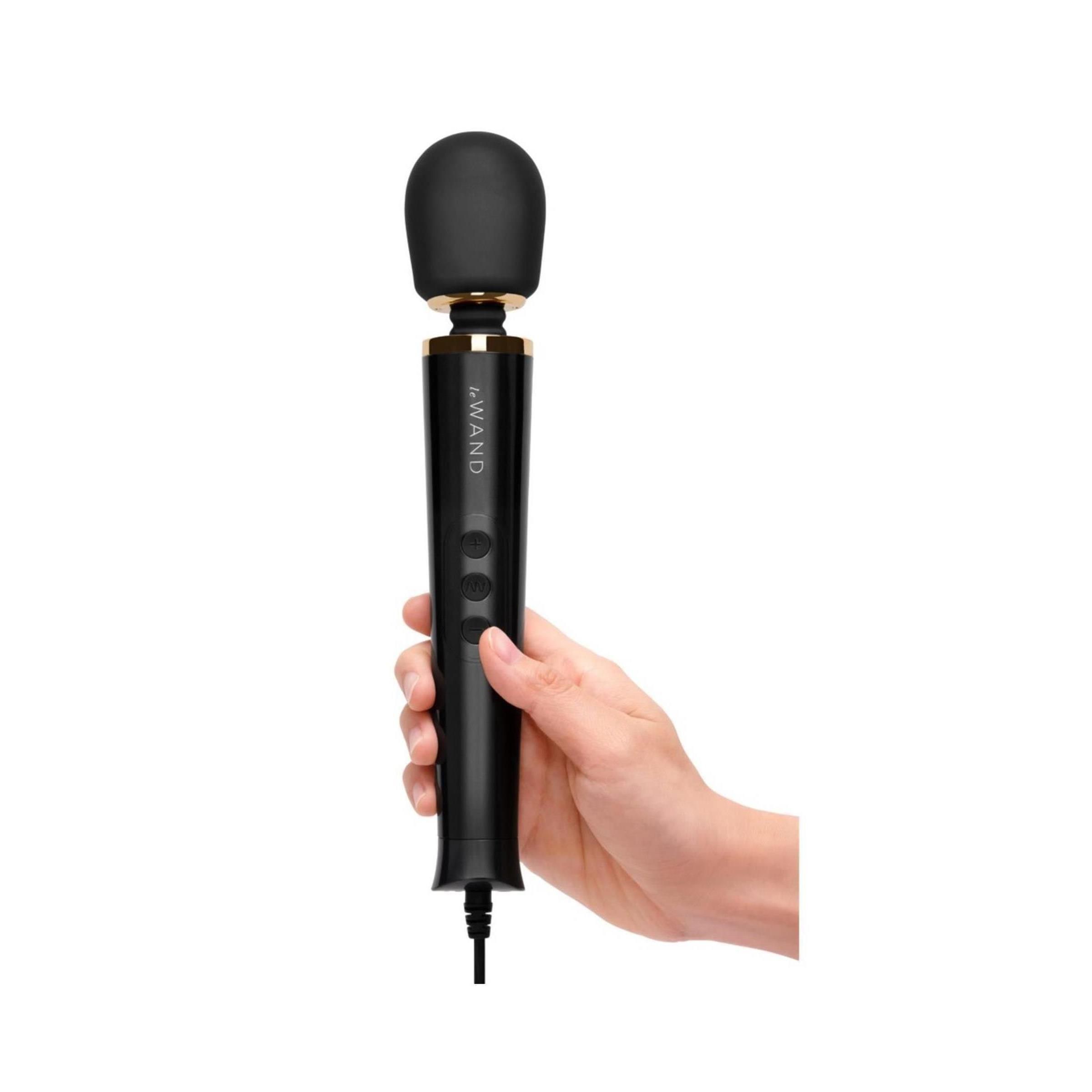 Schwarzer Massagestab in einer Hand gehalten. Abgerundeter Kopf, drei Knöpfe, goldfarbene Akzente. Kabelanschluss.