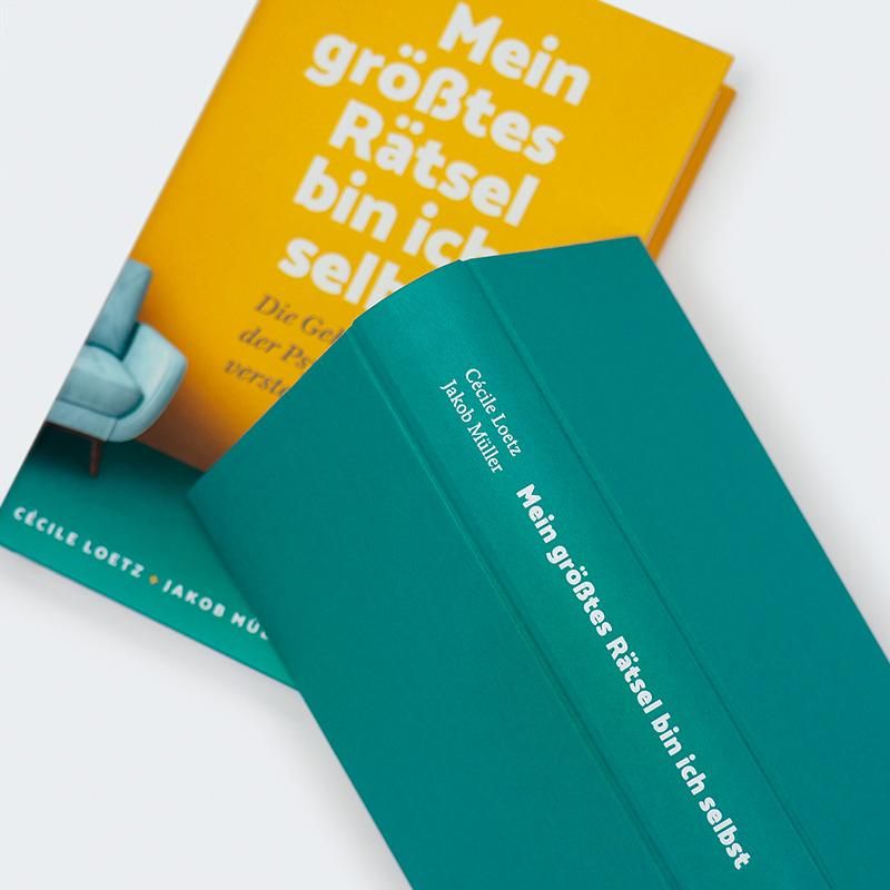 Zwei Bücher: "Mein größtes Rätsel bin ich selbst". Gelbes Cover, grüner Buchrücken. Titel auf dem Buchrücken. Autorennamen.