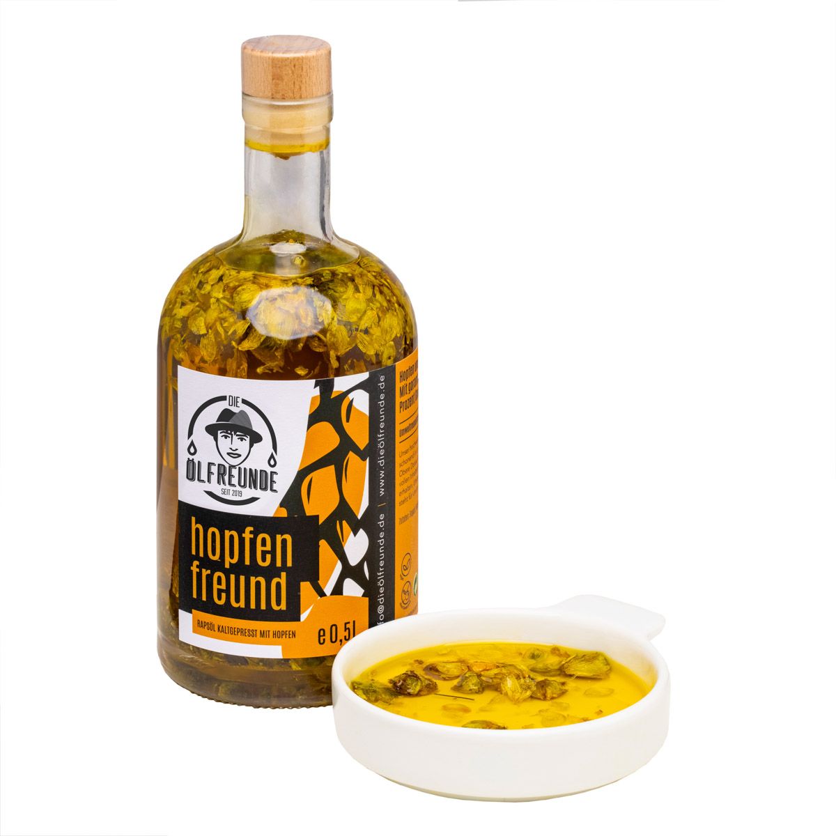 Glasflasche mit gelber Flüssigkeit und Kräutern. Etikett mit Logo und Schriftzug "hopfen freund". Kleine Schale mit Flüssigkeit.