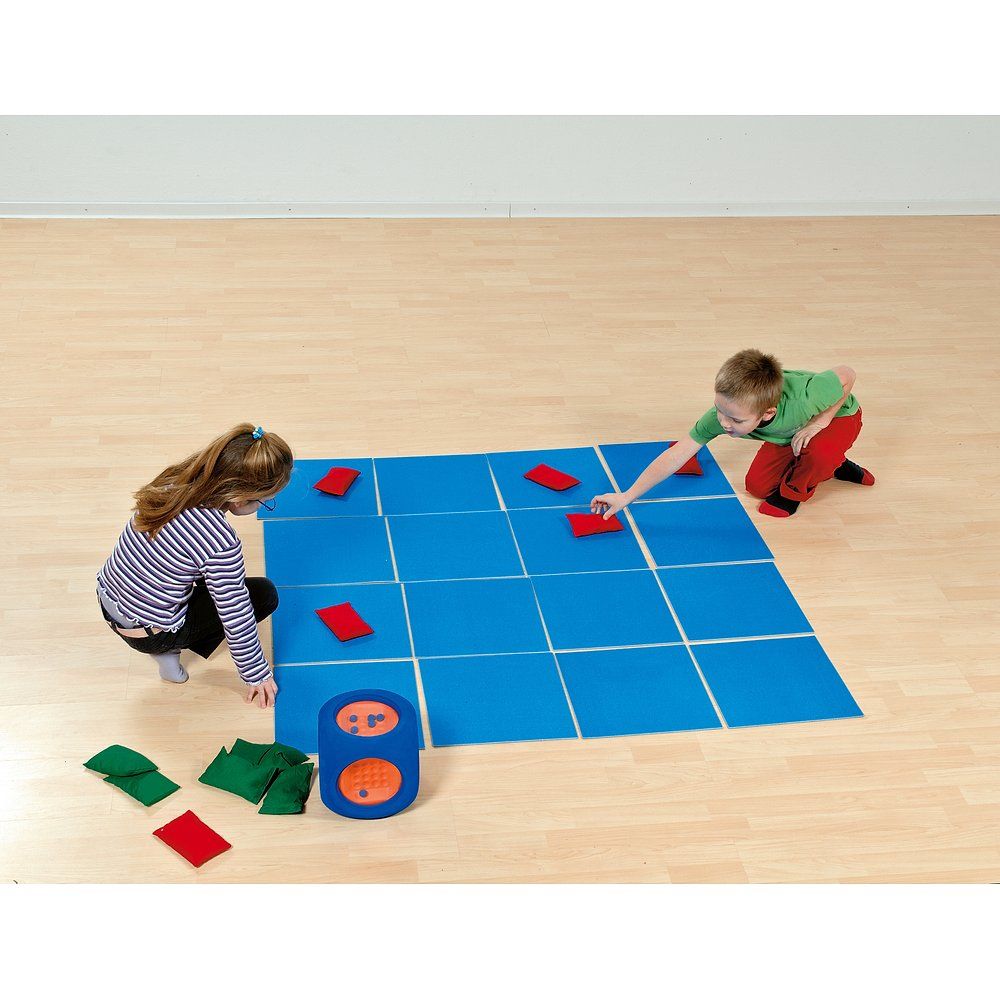 Zwei Kinder spielen mit einem blauen Feld und farbigen Elementen. Ein Würfel liegt am Rand.