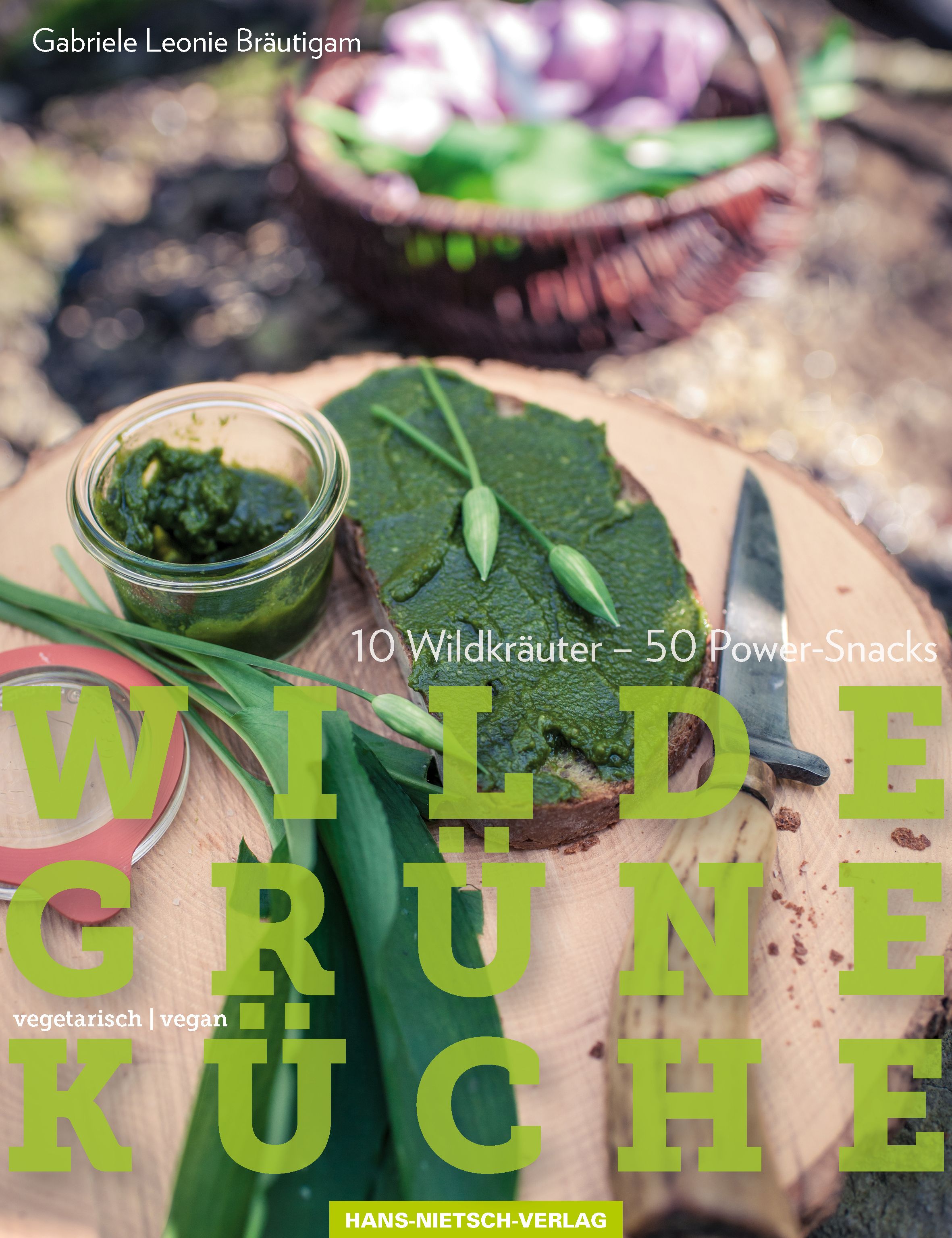 Buchcover mit dem Titel "Wilde Grüne Küche". Es zeigt ein Brot mit Kräuteraufstrich, ein Glas mit Pesto und Kräuter.