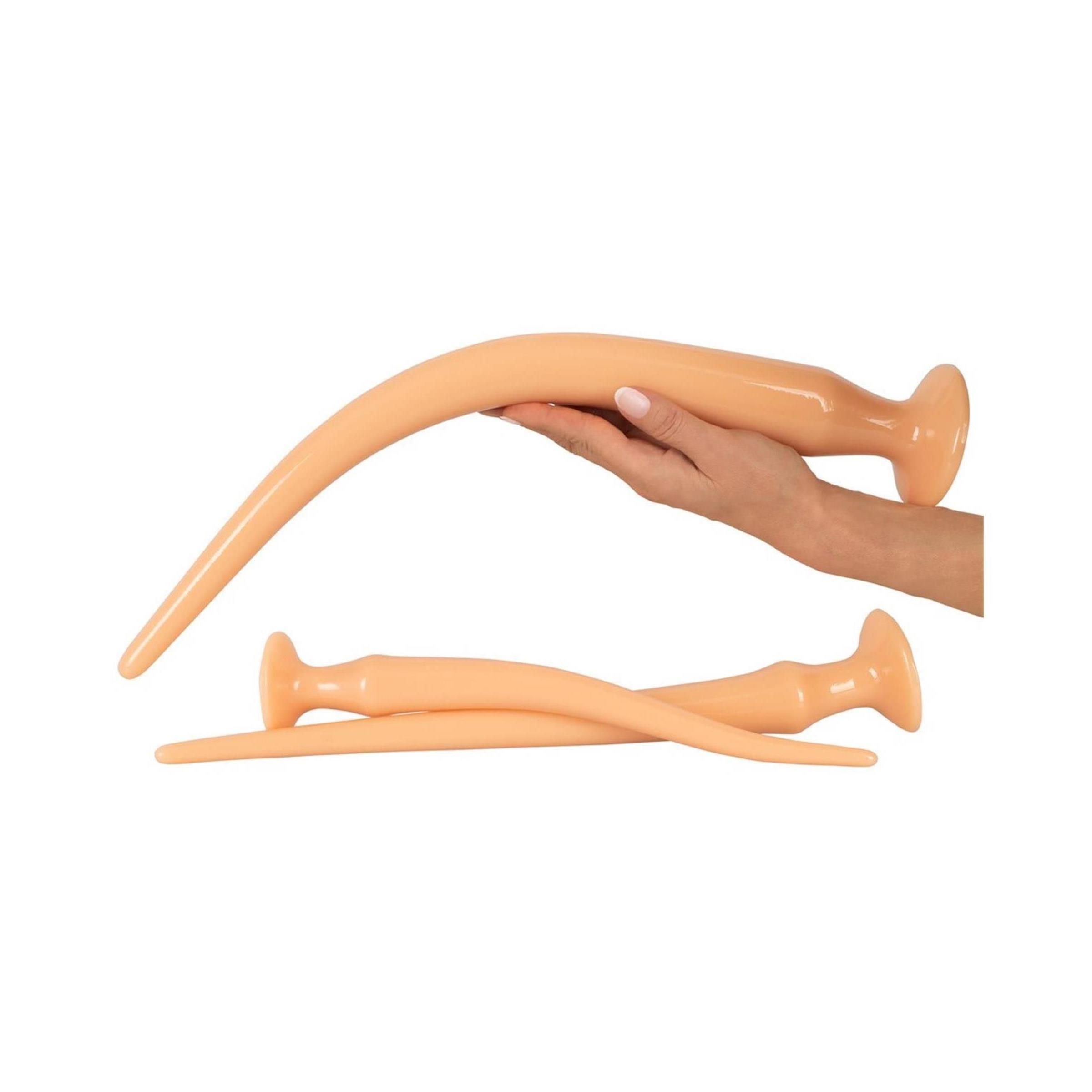 Hand hält ein gebogenes, beige Anal-Plug-Spielzeug. Zwei weitere liegen daneben.