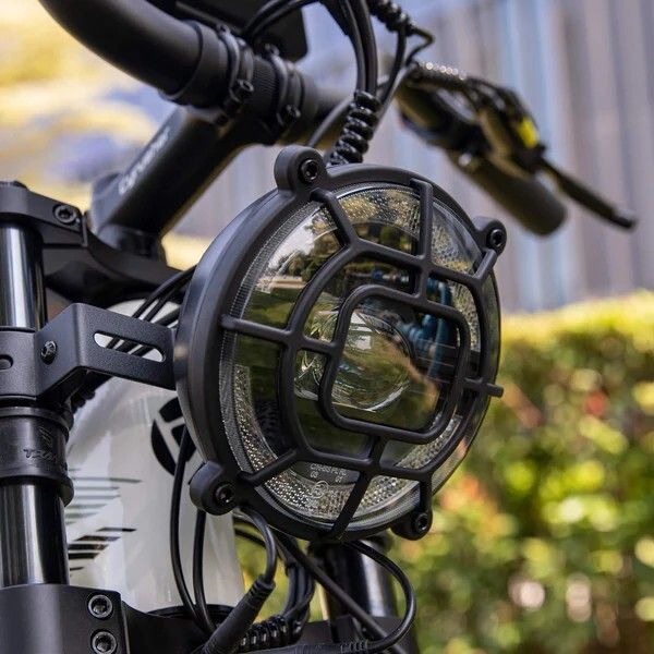 Runder Fahrradscheinwerfer mit Schutzgitter. Schwarzes Gehäuse, klare Linse. An der Gabel befestigt.