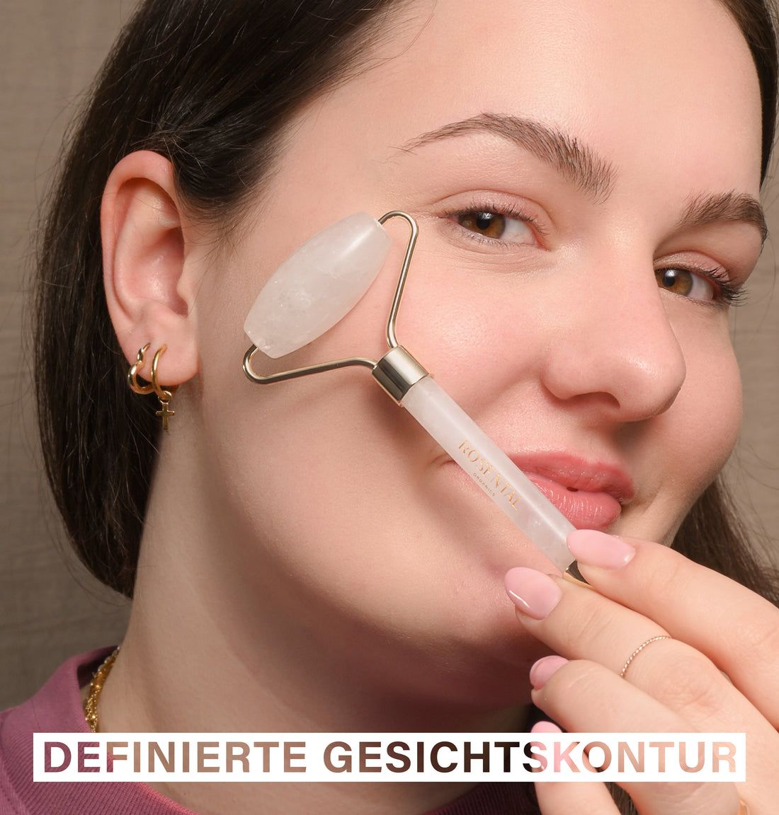 Frau verwendet einen Gesichtsroller auf ihrer Wange. Der Roller hat goldfarbene Halterungen und einen weißen Kristall.