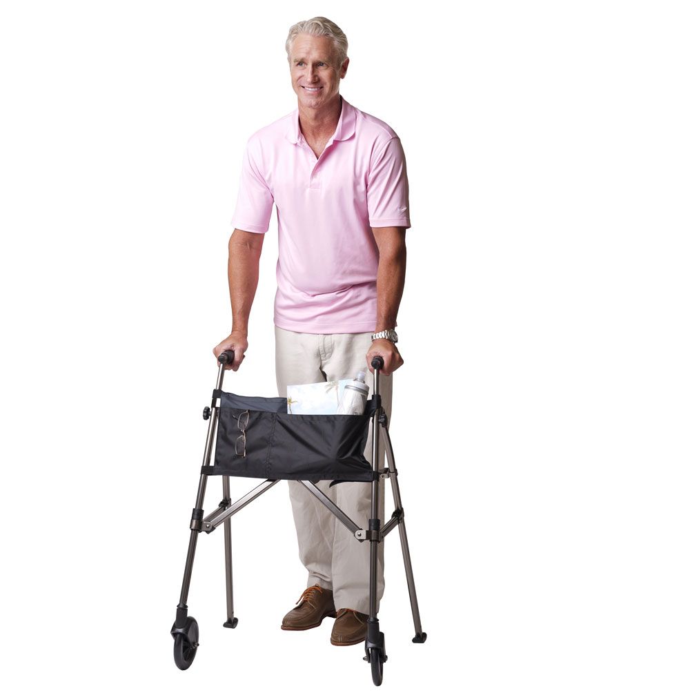 Älterer Mann mit Gehgestell. Steht vor weißem Hintergrund. Rosa Hemd, beige Hose. Gehgestell mit Tasche.