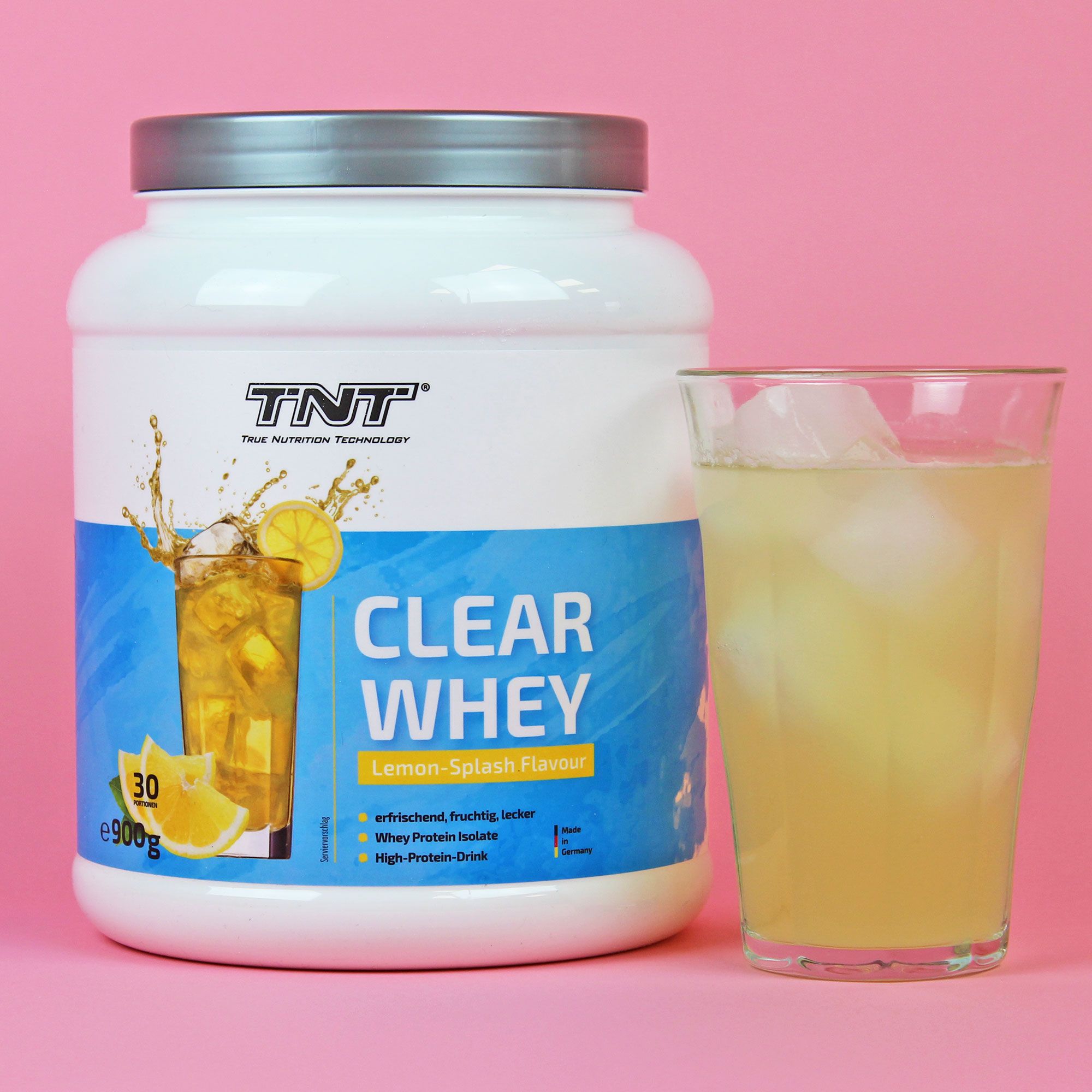 TNT Clear Whey-Dose und Glas mit Getränk. Aufdruck: Clear Whey, Lemon Splash Flavour. Pinker Hintergrund.