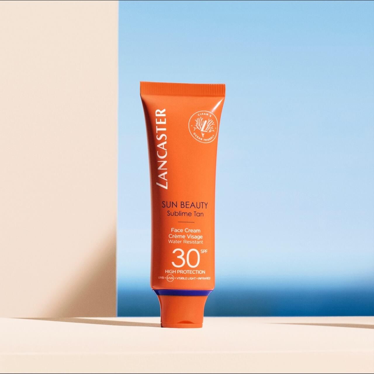 Orangefarbene Tube mit Lancaster-Logo, Sun Beauty, SPF 30. Text: Face Cream, Wasserfest. Hintergrund: blau und weiß.