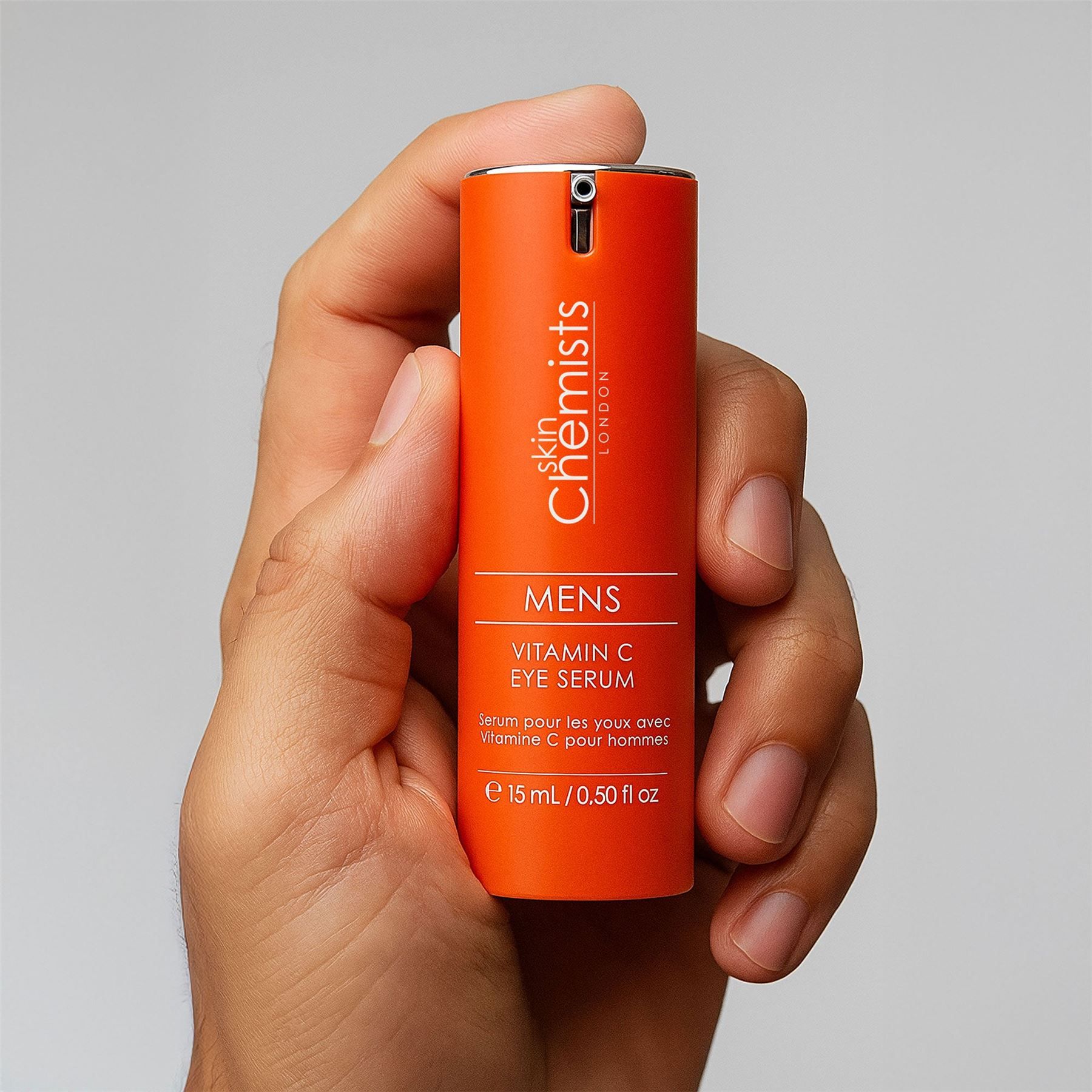 Mann hält eine orangefarbene Flasche des SkinChemists Augenserums mit Vitamin C.