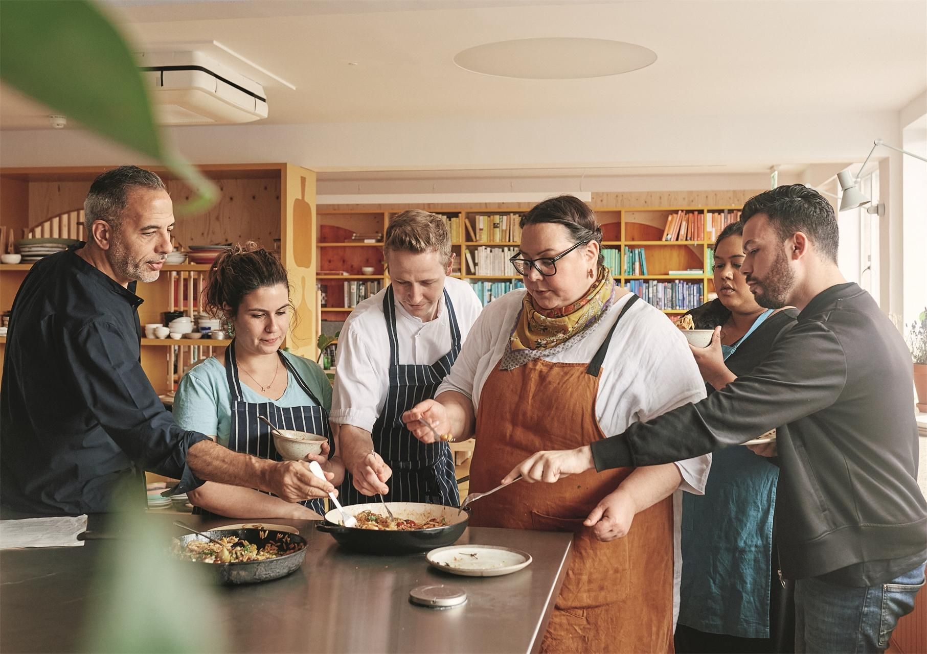 Gruppe von Köchen in einer Küche. Sie bereiten Essen zu. Edelstahl-Arbeitsfläche, Kochutensilien.