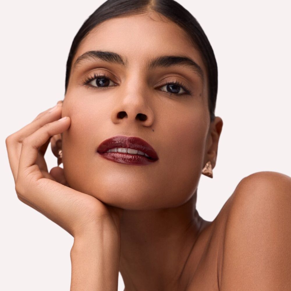 Porträt einer Frau mit dunkelrotem Lippenstift. Sie stützt ihr Kinn auf ihre Hand.