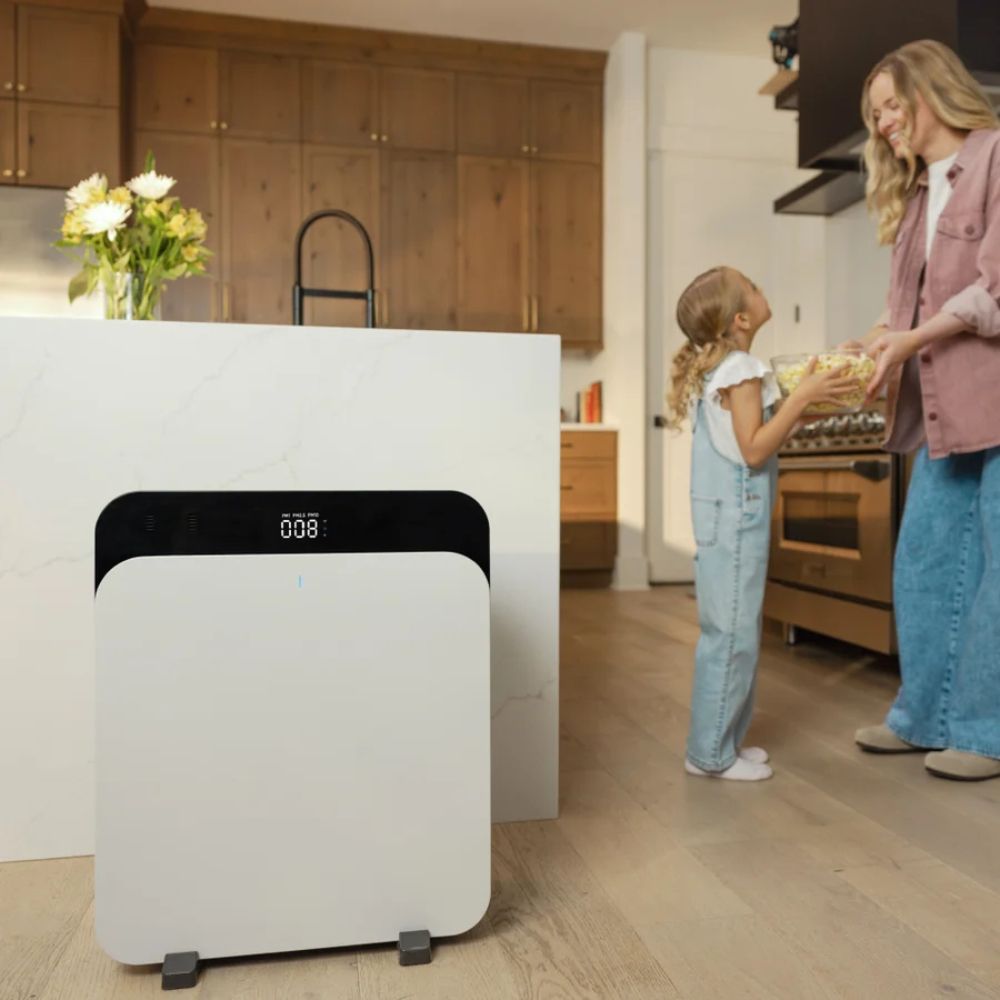 Weißer Luftreiniger mit digitaler Anzeige in Küche. Eine Frau und ein Kind stehen daneben. Schwarzes Oberteil, weiße Front.