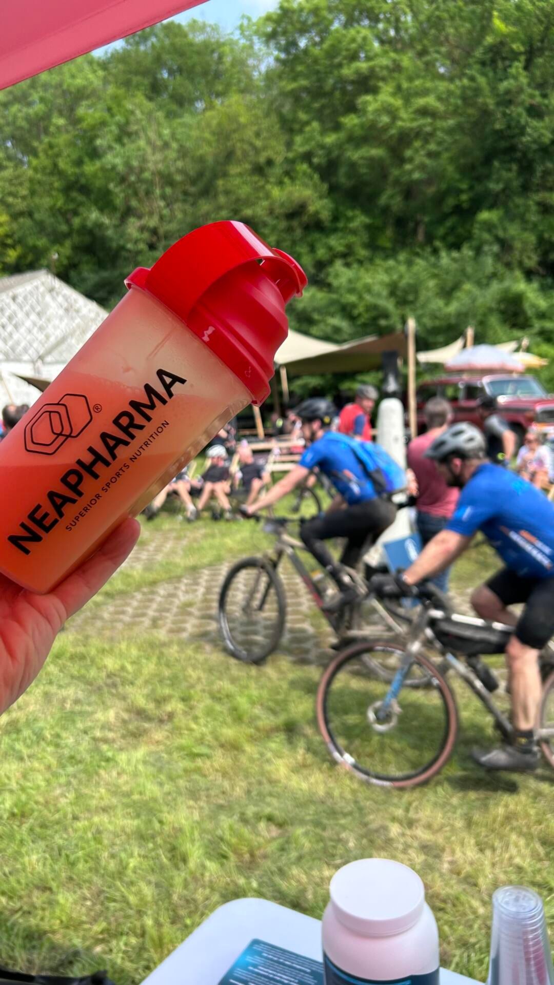 Hand hält Shaker mit orangefarbener Flüssigkeit. Aufgedruckt: Neapharma, Superior Sports Nutrition.