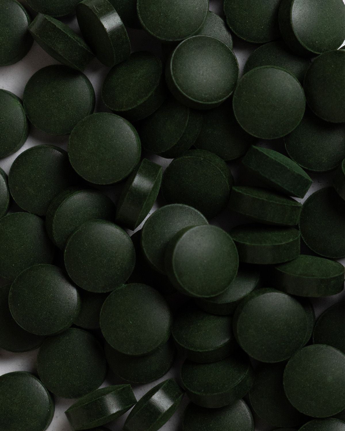 Haufen dunkelgrüner, runder Tabletten. Tabletten sind flach und dicht aneinandergereiht.