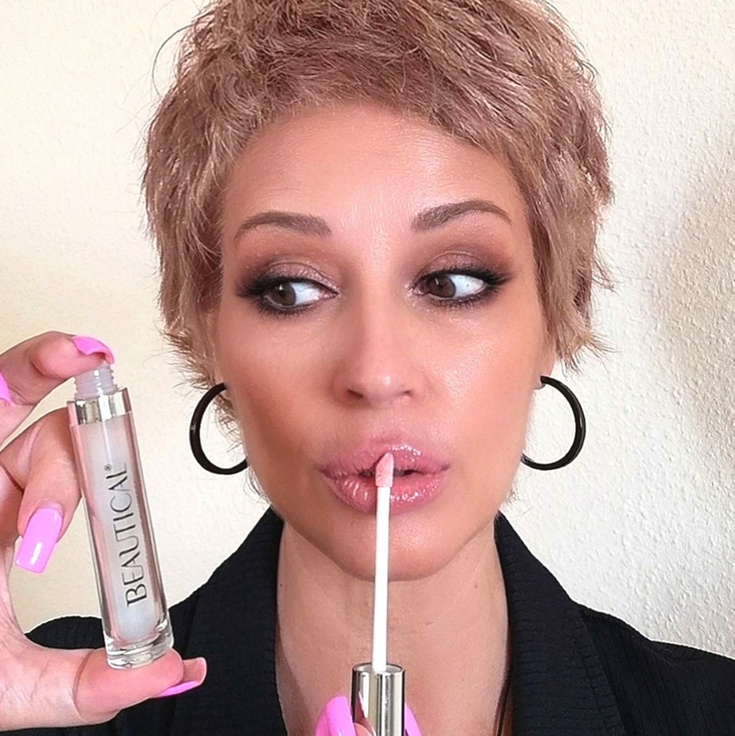 Frau mit Make-up hält BEAUTICAL Instant Lip Plumper. Produkt mit Applikator. Schwarze Ohrringe.