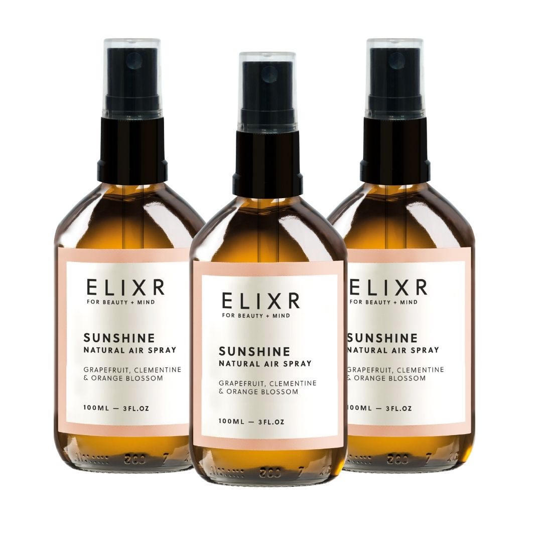 Drei Flaschen ELIXR SUNSHINE Natural Air Spray. Braunes Glas, schwarzer Sprühkopf, weißes Etikett mit Text. Grapefruit, Clementine & Orangenblüte.