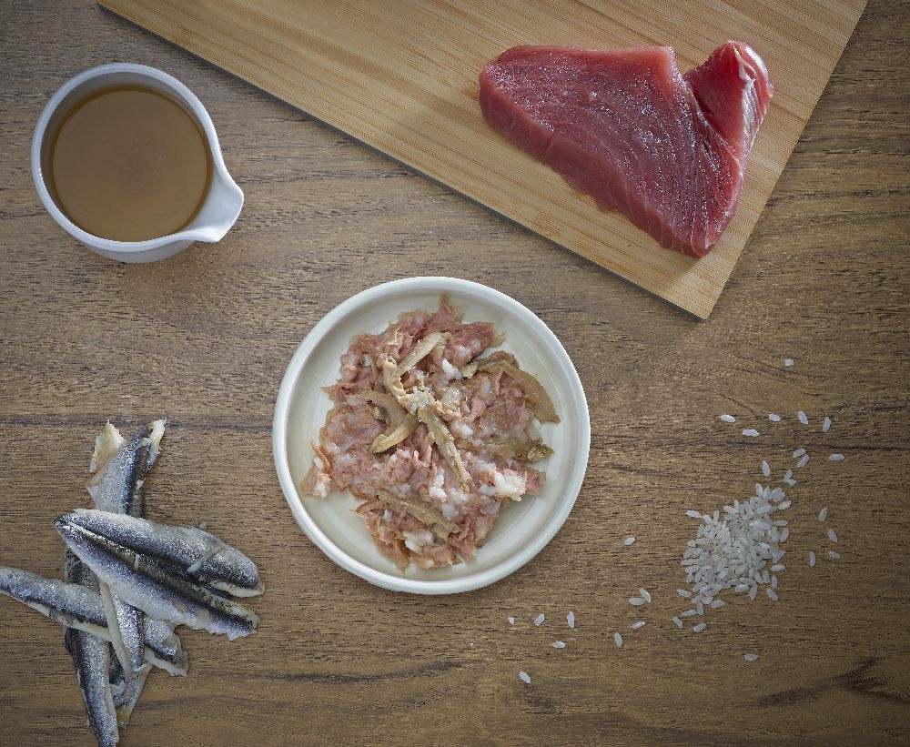 Zubereitung mit Thunfisch, Sardellen, Reis und Sauce auf Holzbrett. Zutaten auf Holzuntergrund angeordnet.